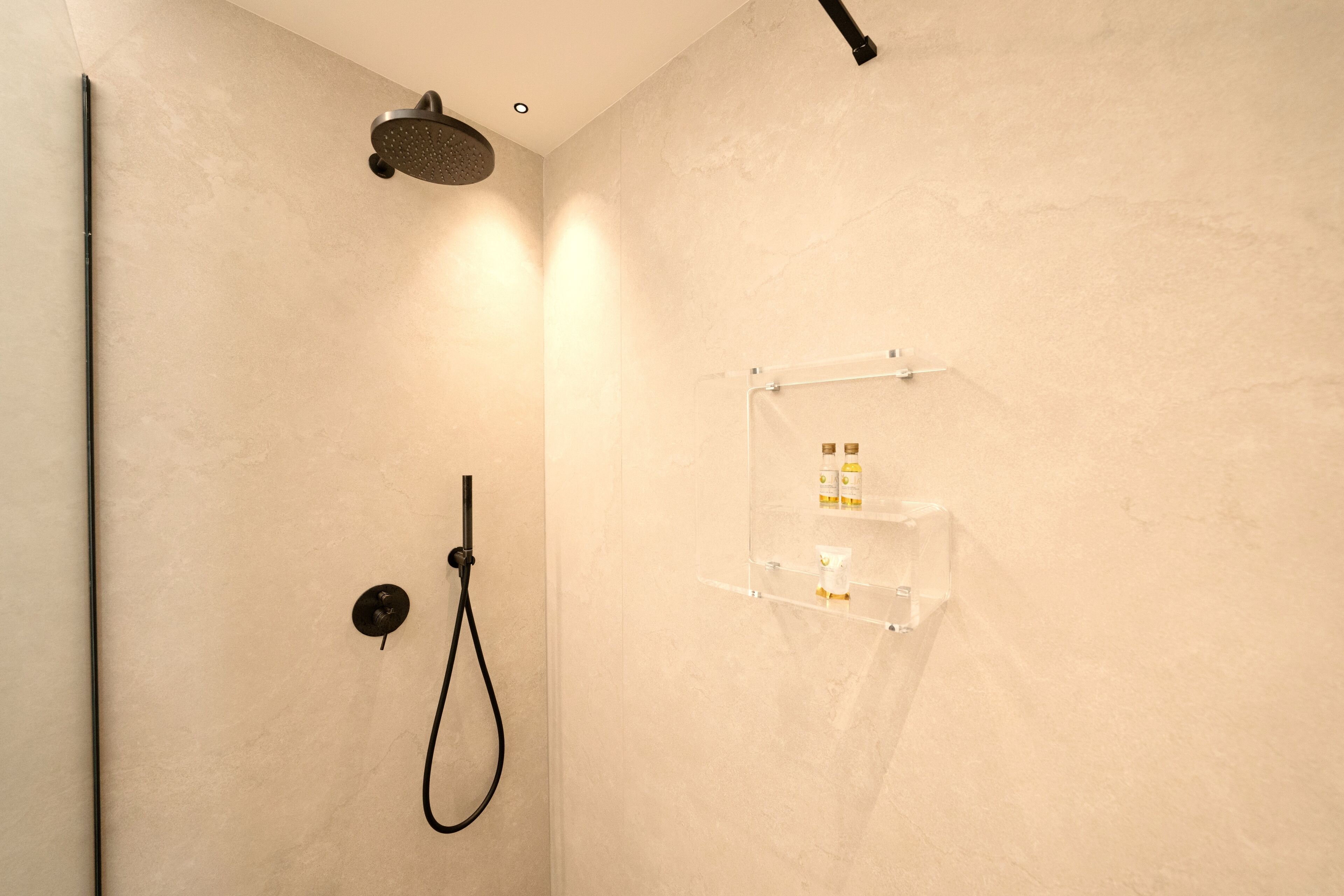 Eine moderne Dusche mit Handbrause und Wandarmatur. Eine klare Ablagefläche für Toilettenartikel ist vorhanden.