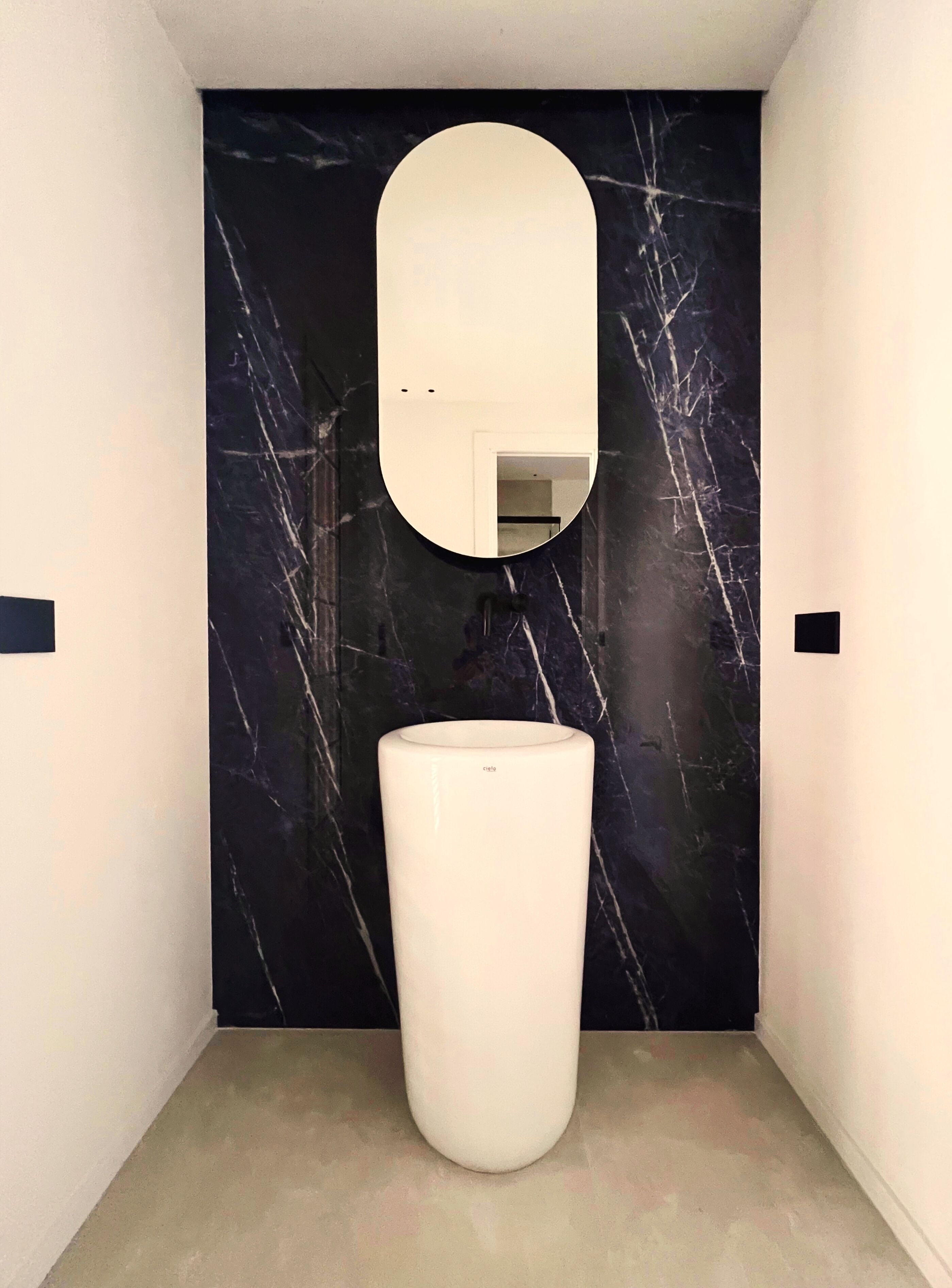 A modern bathroom with a marble wall, a white pedestal sink, and a rectangular mirror.