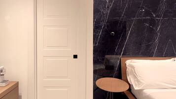 A bedroom with a bed, a small round table, a nightstand, and a wall with a marble-like pattern.