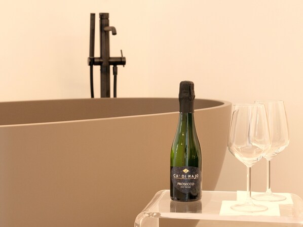 A bottle of wine and two glasses on a clear table against a beige wall.