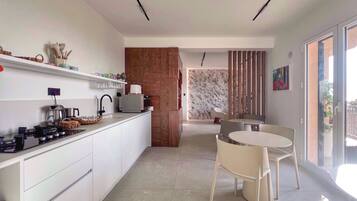 Una cocina moderna con armarios blancos, un comedor con una mesa redonda y sillas, y vistas al exterior a través de un ventanal corredero.