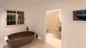 Een moderne badkamer met een vrijstaand bad, een raam met geëtste glas en een schilderij van boten aan de muur.