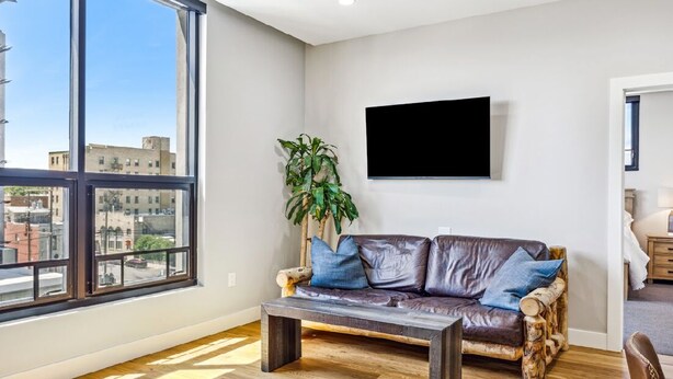 Una sala de estar moderna con un sofá de cuero, una mesa de centro de madera y un amplio ventanal con vistas a la ciudad.