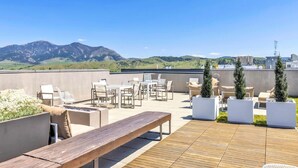 Una terraza en la azotea con mobiliario exterior, macetas y vistas a montañas.