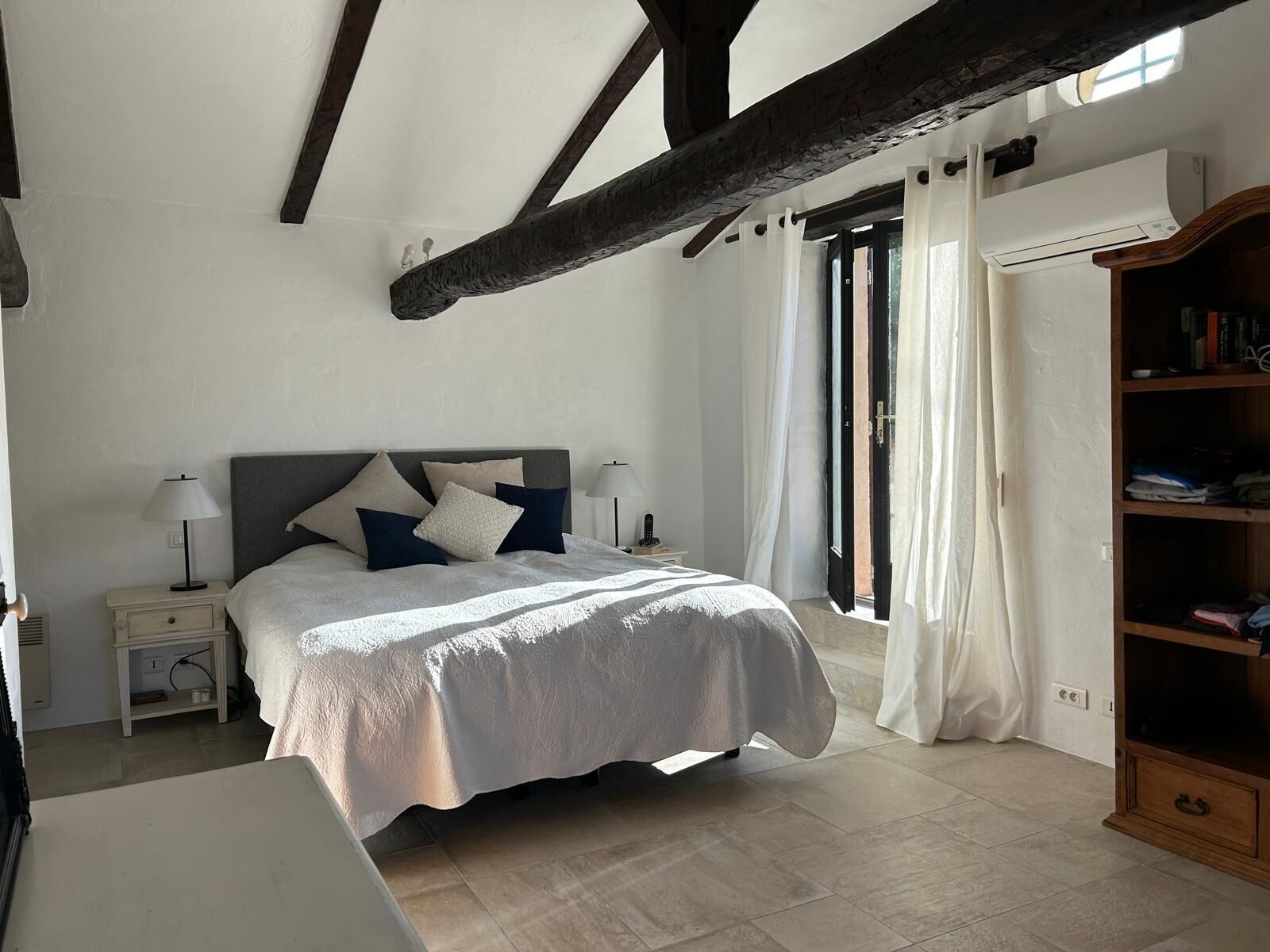A bedroom with a bed, nightstands, a wooden wardrobe, and a window with curtains.