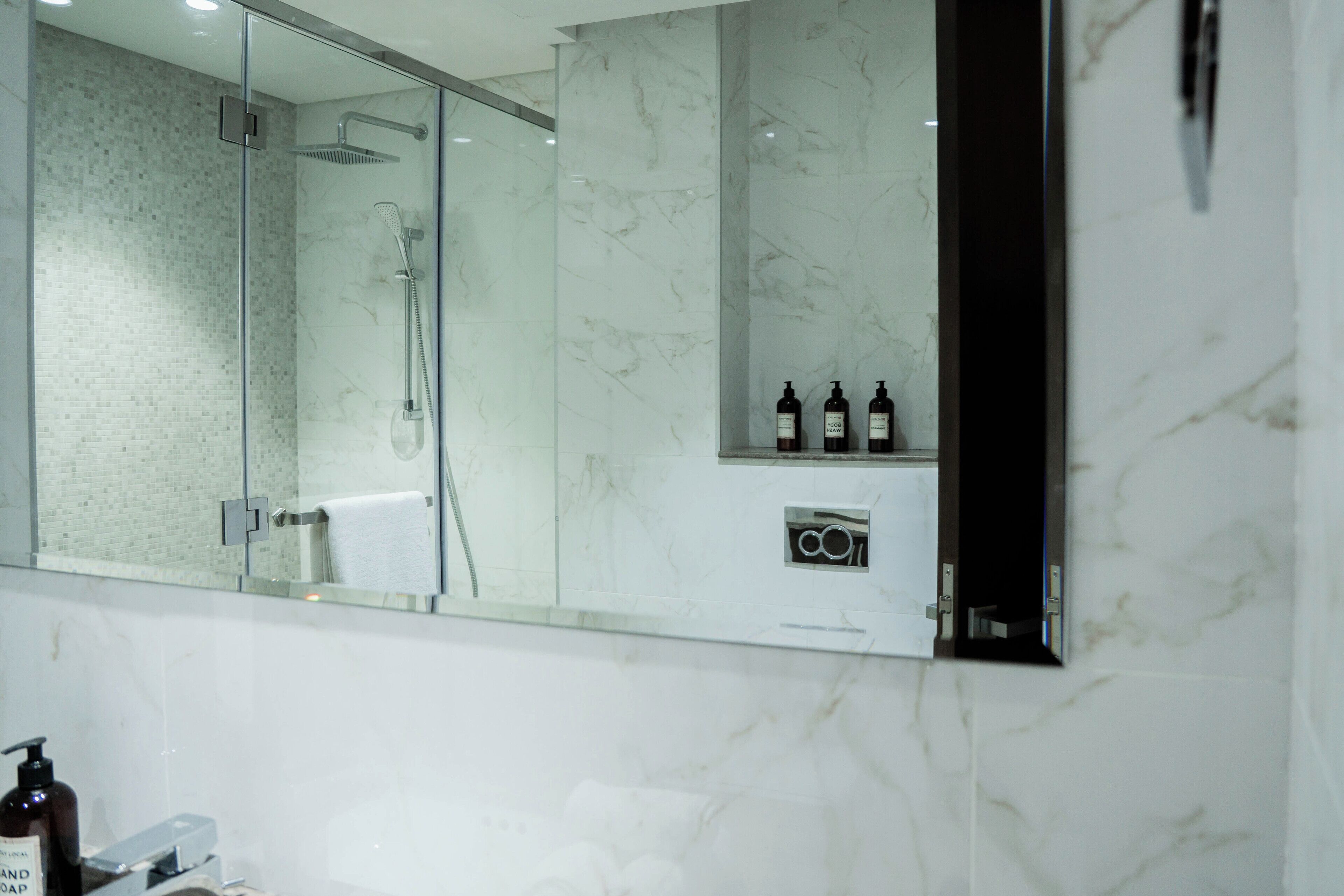 A modern bathroom with a glass-enclosed shower, marble walls, and a mirror reflecting the space.
