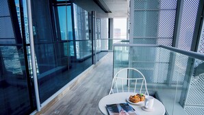 Un balcon moderne avec une balustrade en verre, une chaise blanche, une table avec un magazine, une assiette contenant de la nourriture et une tasse.