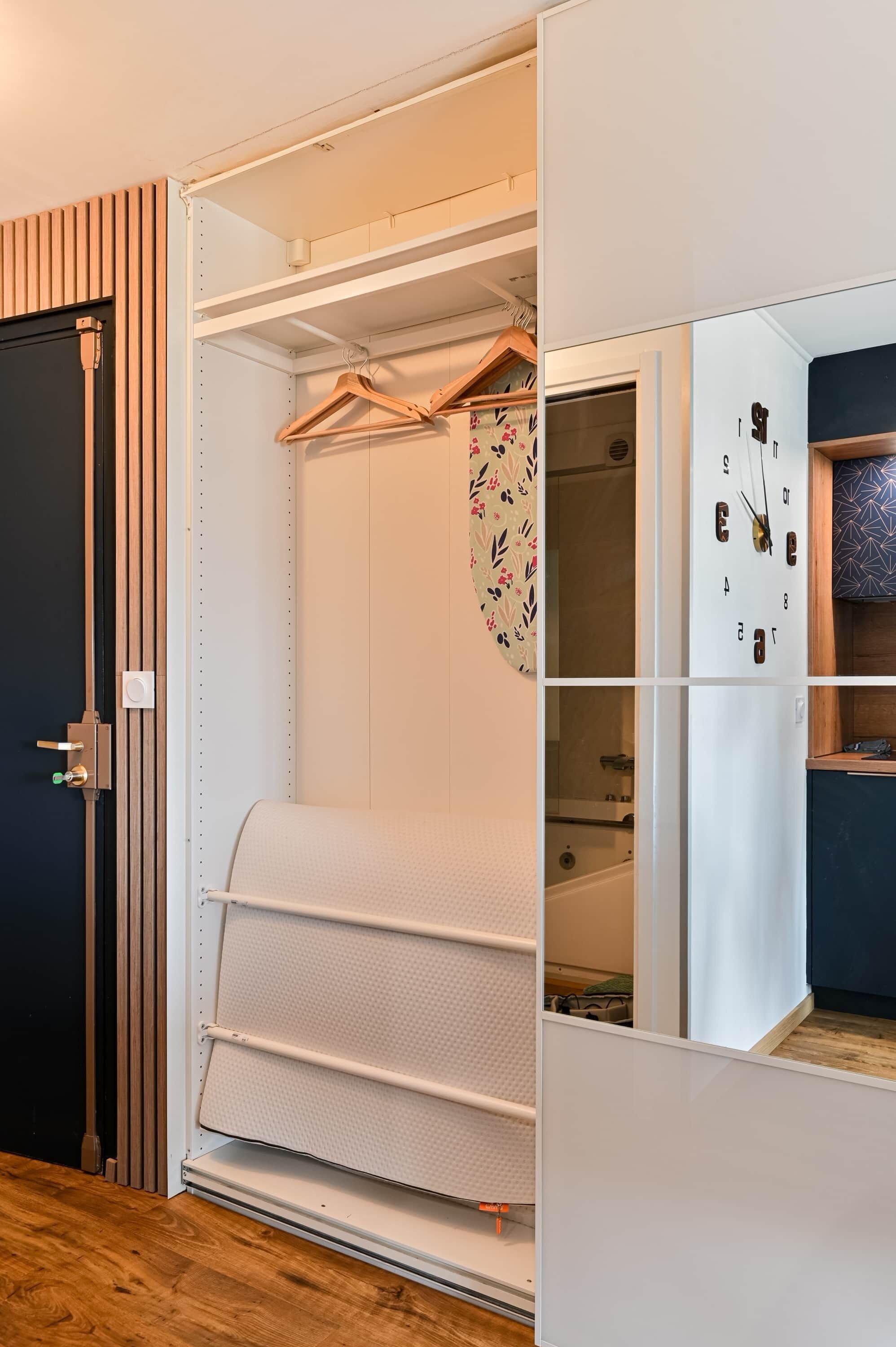 Un dressing avec une tringle à vêtements, une porte de placard miroir et un appareil électroménager intégré.