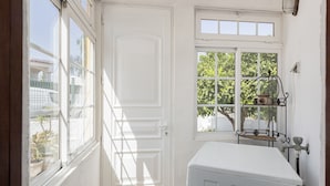 Ein Badezimmer mit weißem Waschbecken, einem Fenster mit Blick ins Grüne und einer Tür.