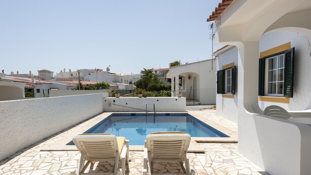 Ein Swimmingpool mit zwei Liegestühlen, einer gefliesten Terrasse und Blick auf umliegende Gebäude.