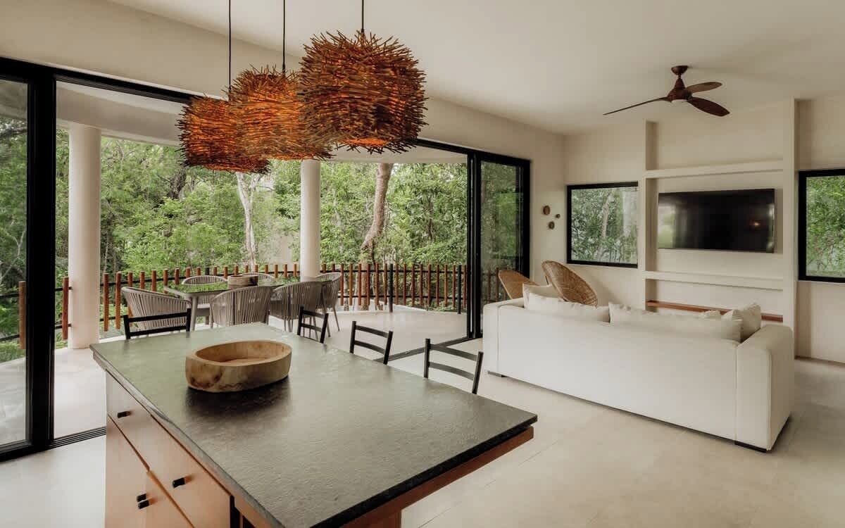 Un salon moderne comprenant un coin repas, de grandes fenêtres, un canapé blanc et un ventilateur de plafond.