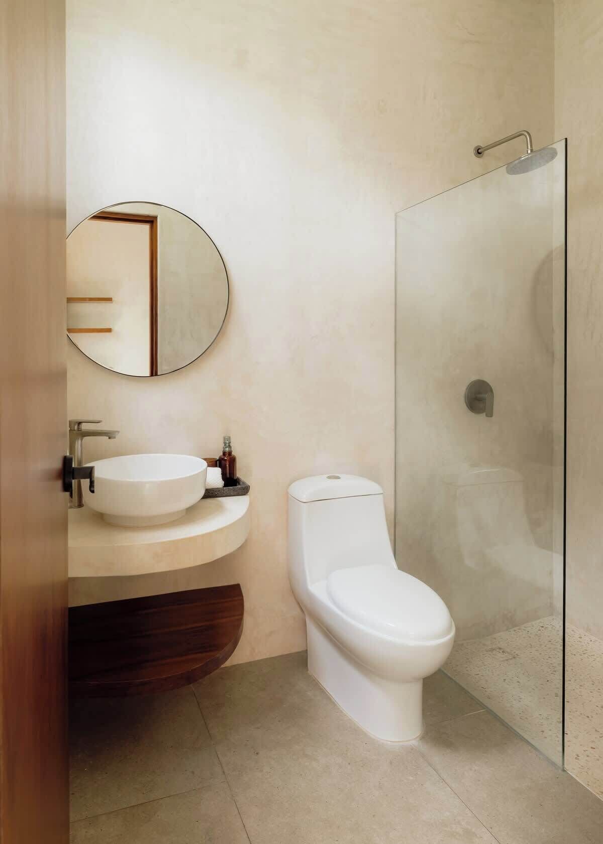 A modern bathroom with a round mirror, a sink, a toilet, and a glass-enclosed shower.