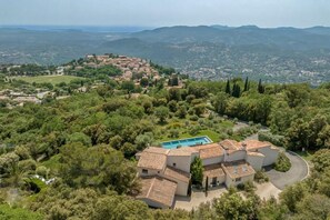 A villa with a swimming pool, surrounded by lush greenery and overlooking a valley.
