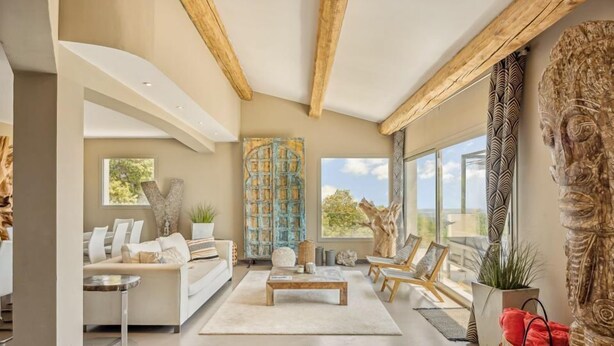 Ein großzügiges Wohnzimmer mit modernem Design, das ein großes Fenster, eine Holzbalkendecke und verschiedene Sitzmöglichkeiten bietet.