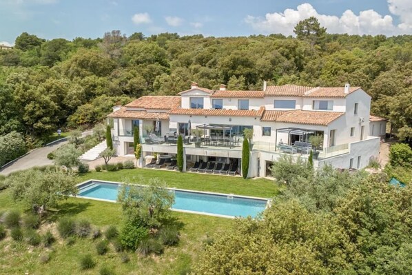 A modern villa with a swimming pool, surrounded by lush greenery and hills.