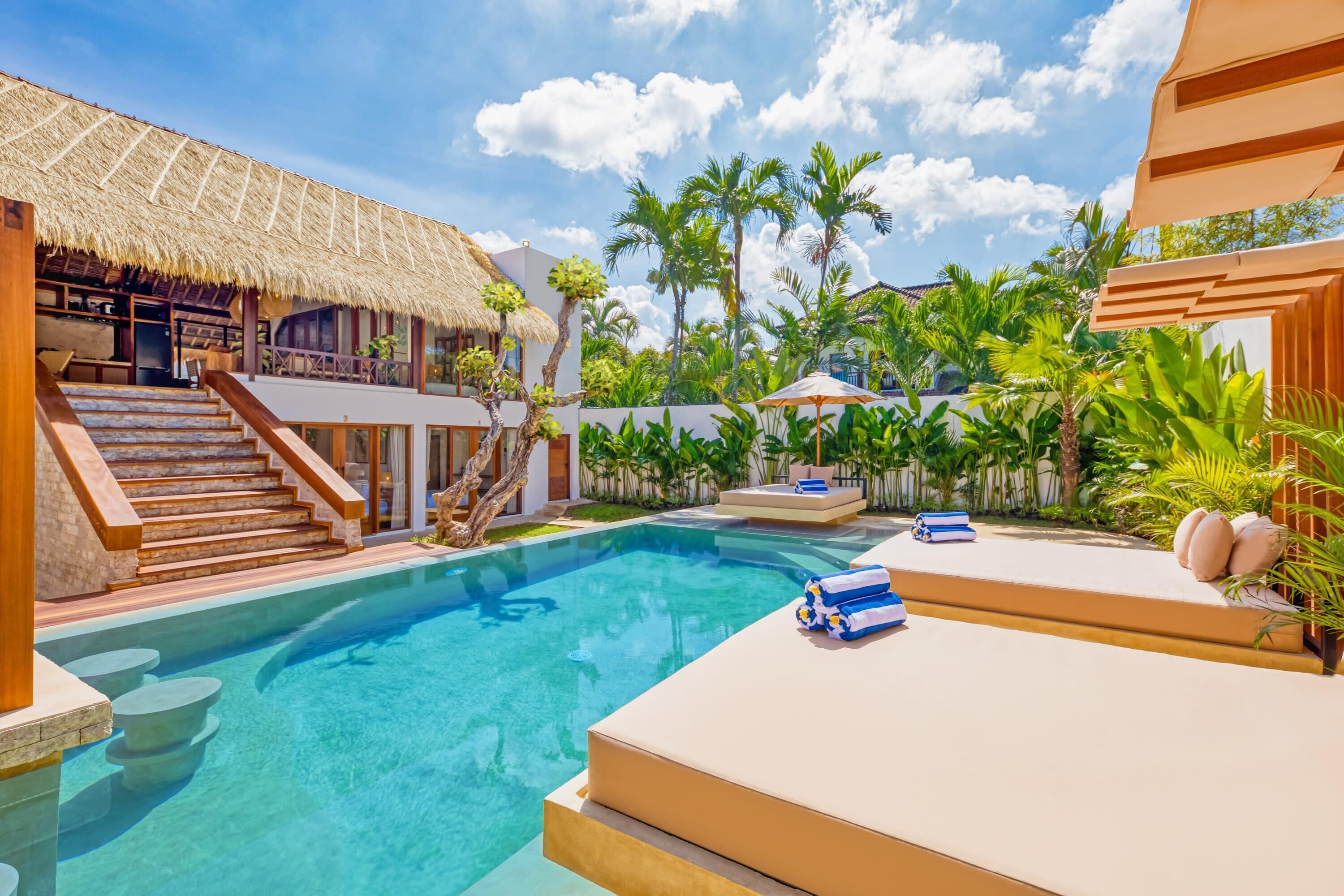 A pool area with a thatched-roof structure, a staircase, and lounge chairs.