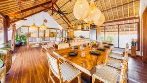 Un comedor amplio con una gran mesa de madera, sillas de mimbre y lámparas colgantes de mimbre.