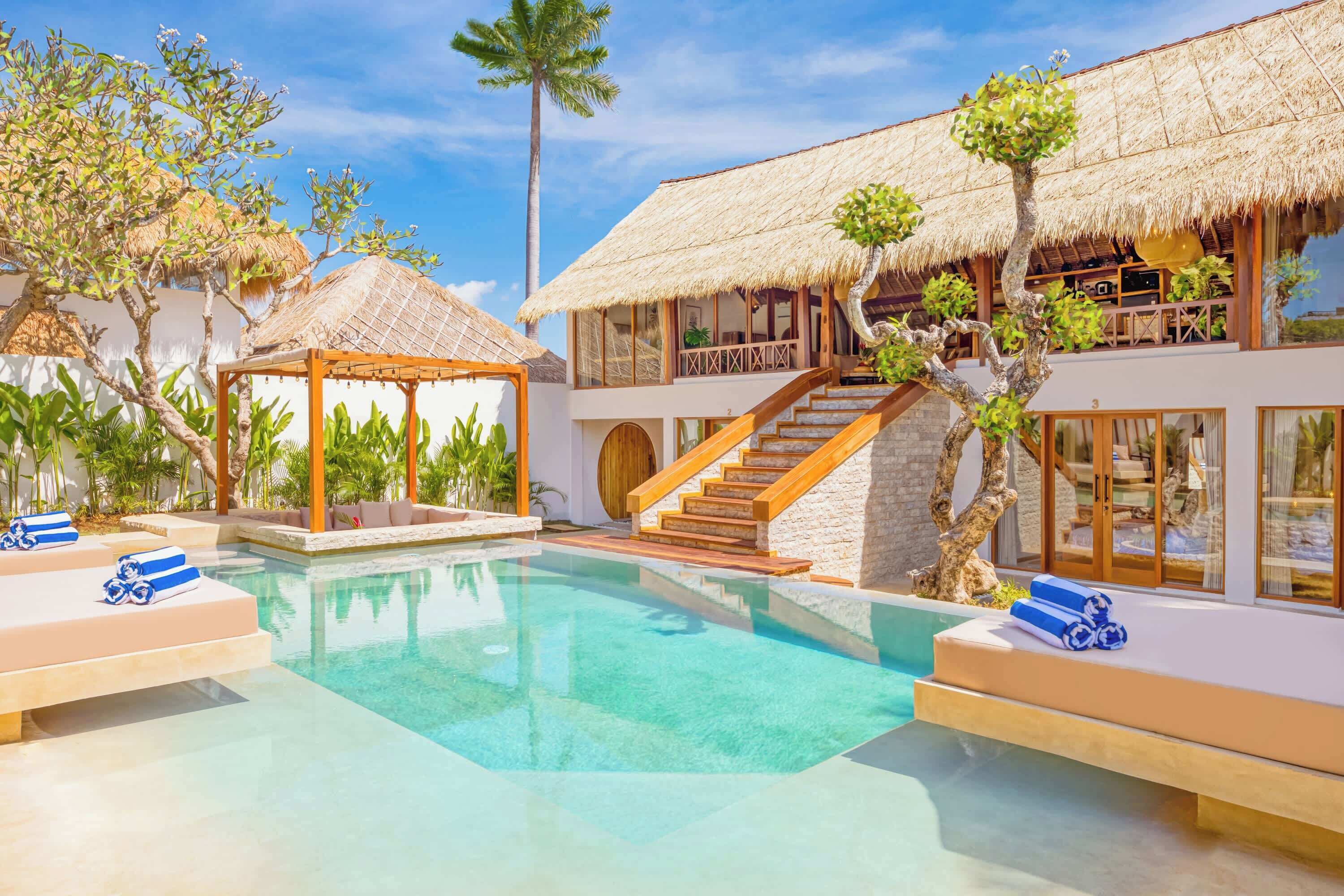 Un complejo turístico con piscina, construcciones de techo de paja y una escalera que conduce a un segundo nivel.
