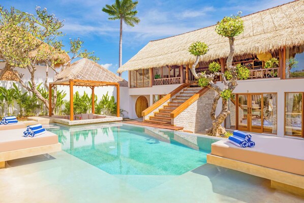 A resort with a swimming pool, thatched-roof structures, and a staircase leading to a second level.