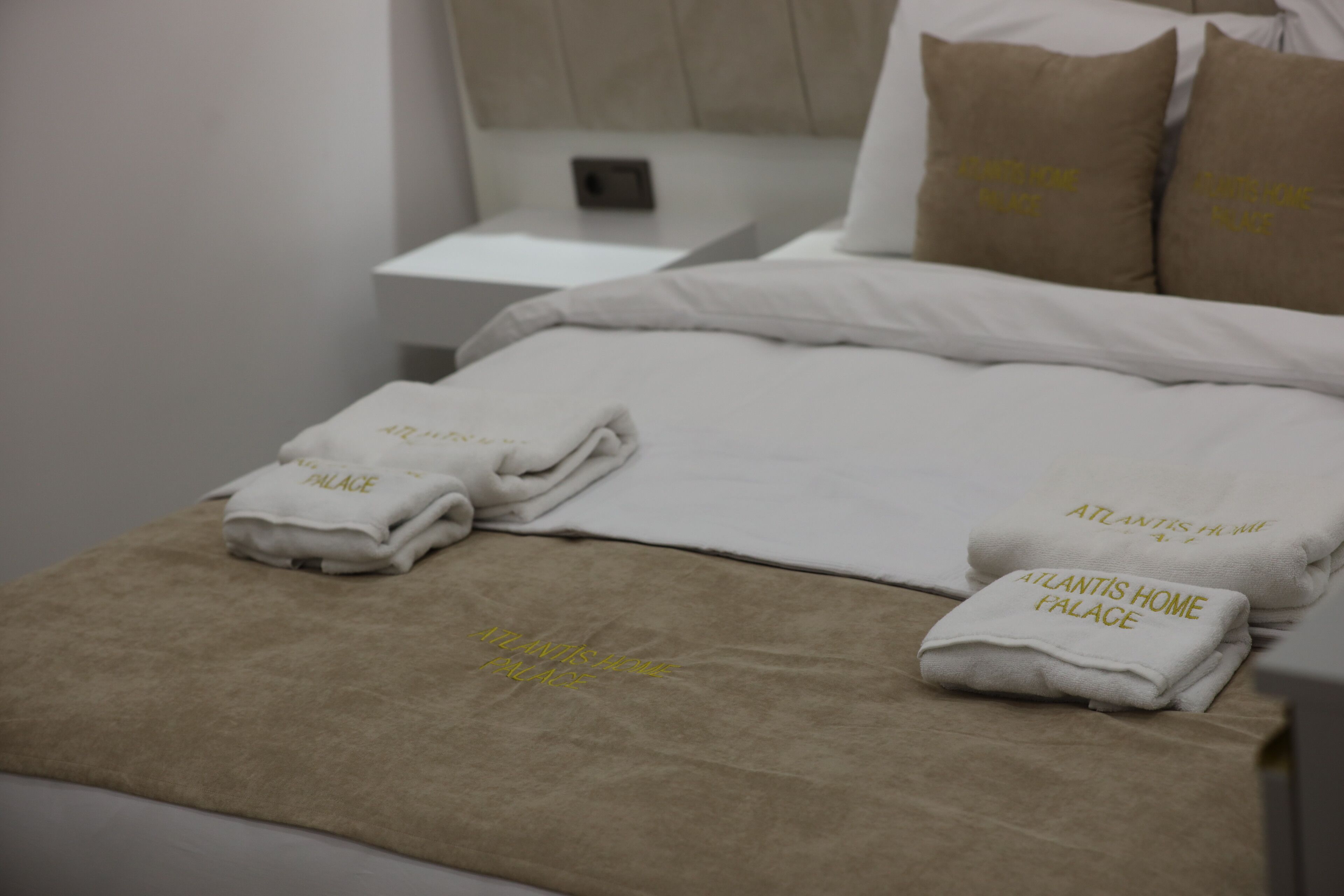 Una cama bien hecha con ropa de cama y toallas blancas, cada una con la etiqueta 'Atlantis Home Palace'.