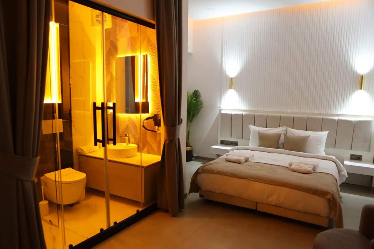 Hotellihuone, jossa on suuri sänky, yöpöytä, pieni sivupöytä, peili, pyöreä pesuallas ja wc.