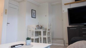 A modern living room with a white sofa, a dining table with chairs, a TV on a stand, and a small plant on the table. - Cozy Tromsø Apartment Near City Center (Tromsø)