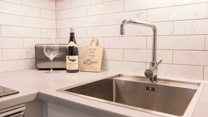A modern kitchen with a stainless steel sink, a wine glass, and a bottle of wine on the counter. - Cozy Tromsø Apartment Near City Center (Tromsø)