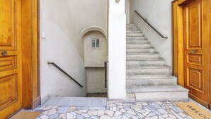 A narrow hallway with a staircase leading to an upper level, wooden doors on either side, and a small window at the top of the stairs. - Terrazze tra i musei - Studio 7B (Naples)