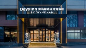 The exterior of Days Inn by Wyndham, featuring a modern entrance with a revolving door, illuminated by vertical lights, and flanked by two elephant statues.