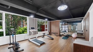 A modern gym with exercise equipment, large windows, and a view of greenery.