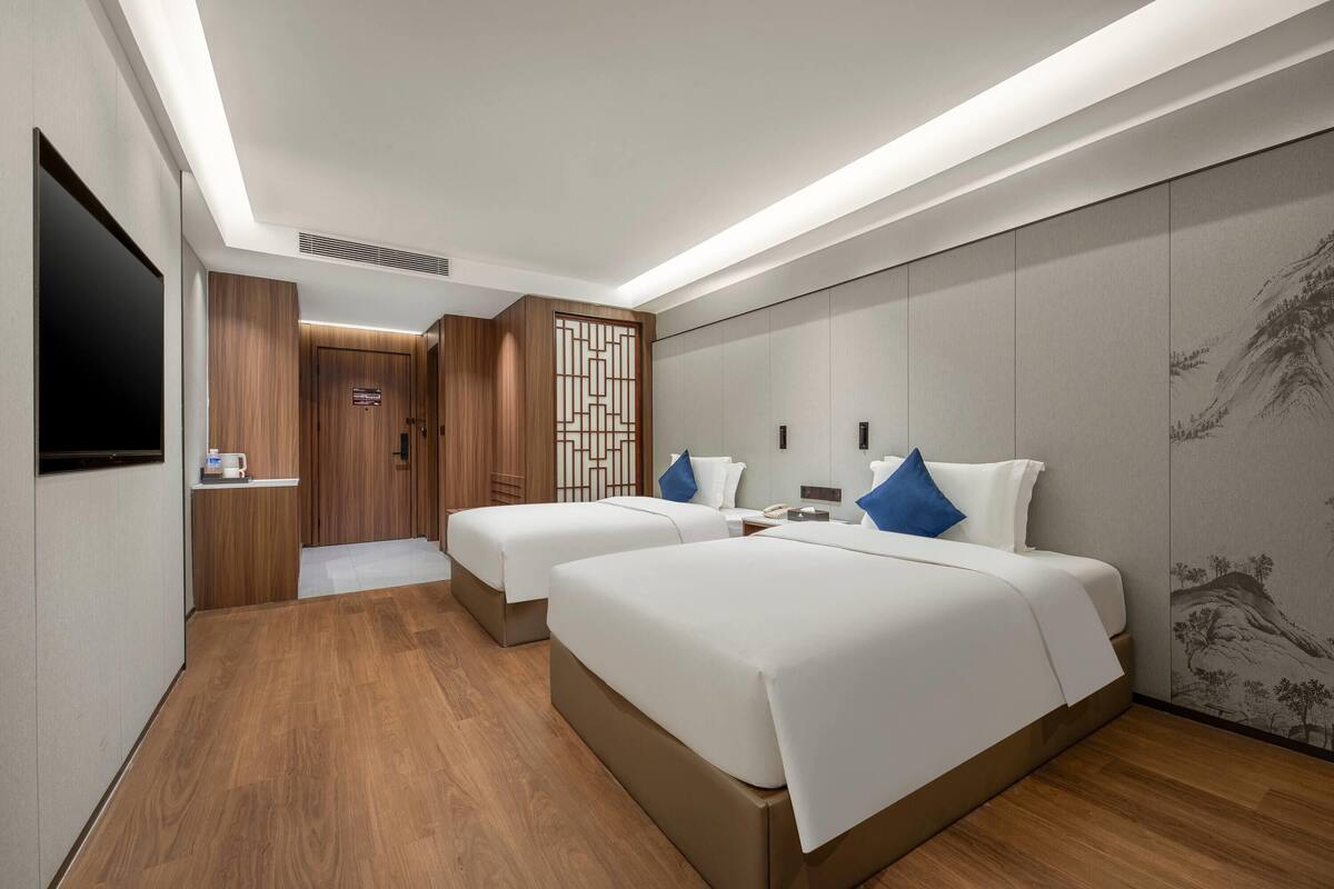 A hotel room with two beds, a TV, a desk, and a decorative wall.