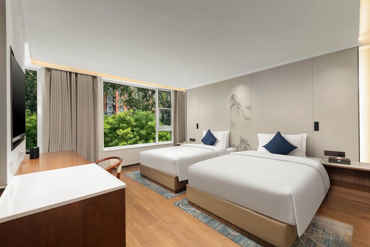 A hotel room with two beds, a desk, and a TV.