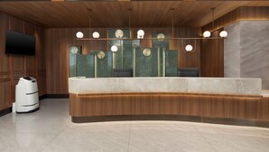 A reception desk with a wooden finish, a flat-screen TV mounted on the wall, and a modern light fixture above.