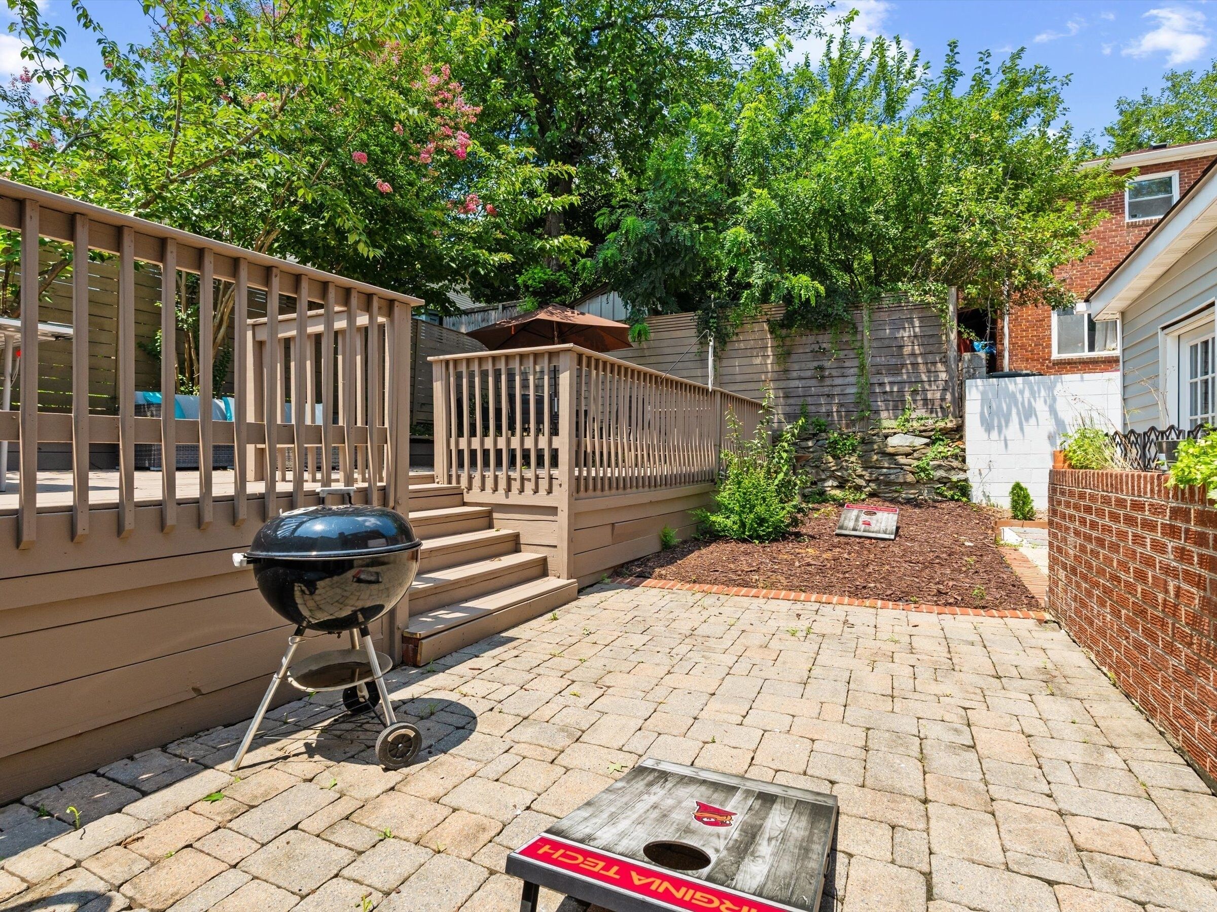 Un patio trasero con una parrilla, escalones de madera y una mesa de madera.