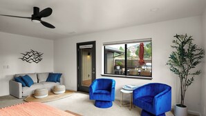 A modern living room with a sofa, two blue armchairs, a coffee table, a large window, and a ceiling fan. - Sedona Retreat • Newly Renovated 3BR Home - Amazing Views (Sedona)