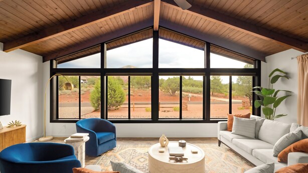 A modern living room with a large window, a blue armchair, a white sofa, and a round coffee table. - Sedona Retreat • Newly Renovated 3BR Home - Amazing Views (Sedona)