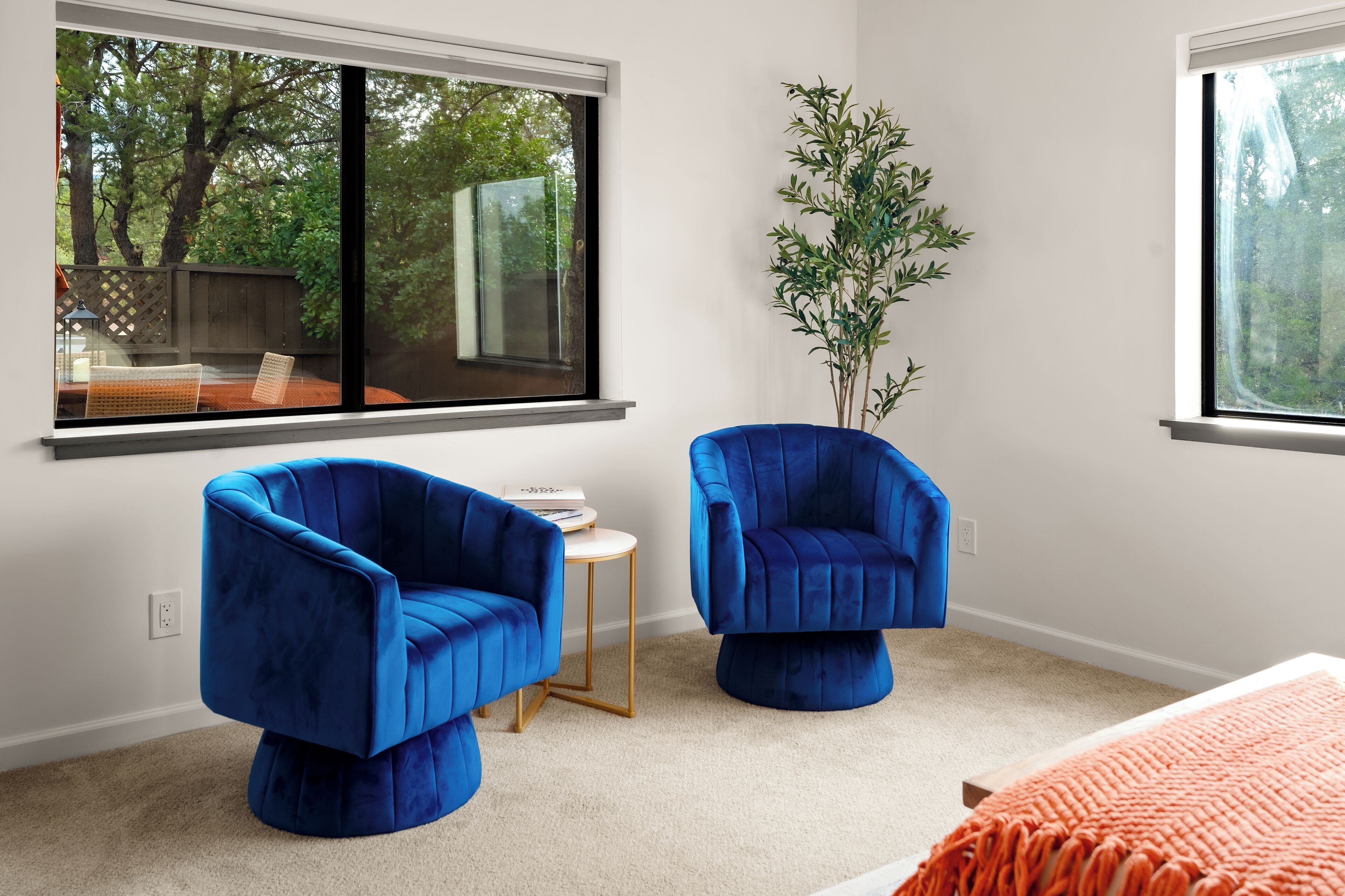 Una habitación moderna con dos sillones azules, una mesita redonda y un ventanal con vistas a árboles.