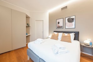 A hotel room with a bed, bedside tables, a wardrobe, and artwork on the wall.