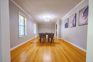 Un comedor con piso de madera, una mesa con sillas y tres obras de arte enmarcadas en la pared.