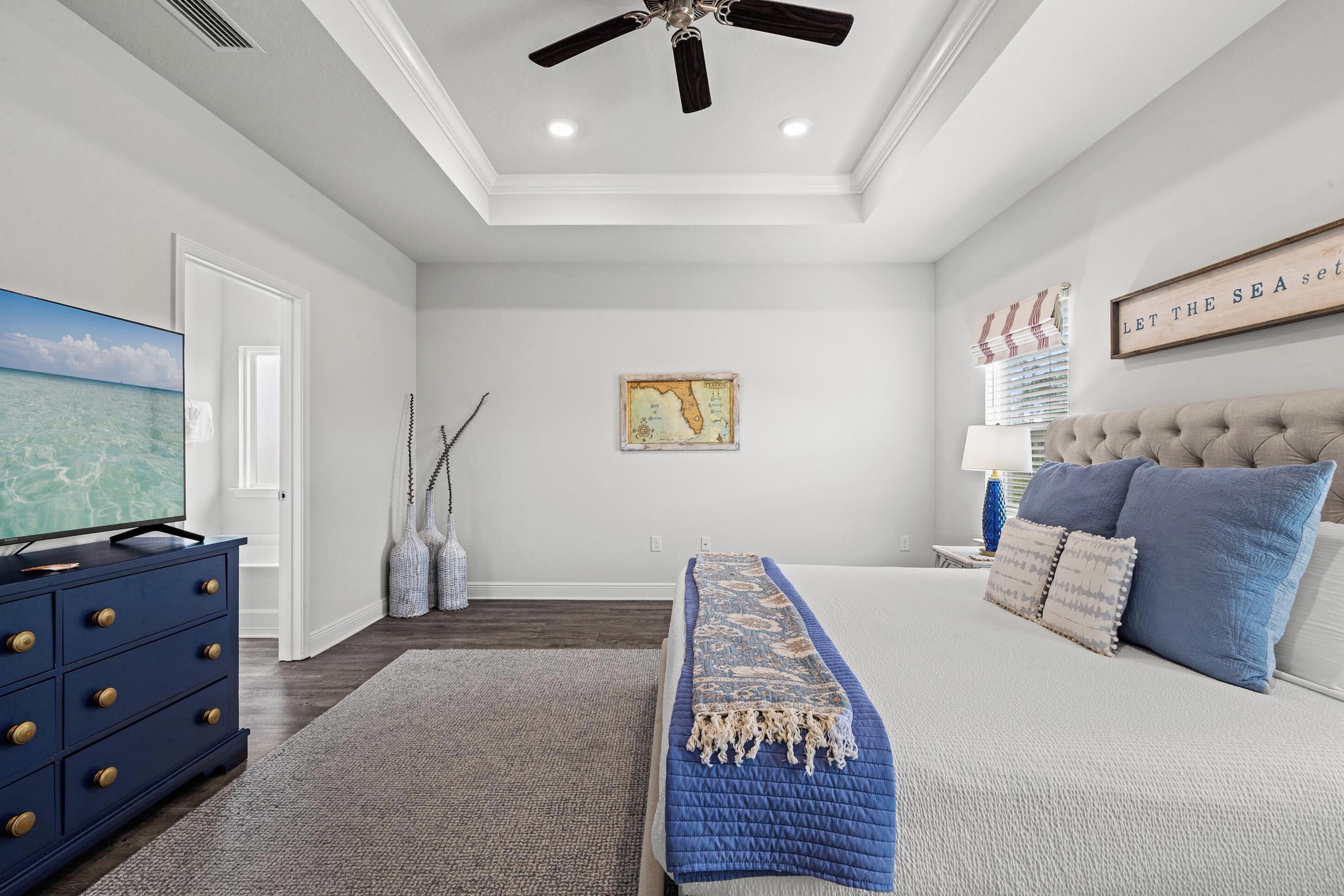 A bedroom with a bed, a dresser, a ceiling fan, a map on the wall, and a television.
