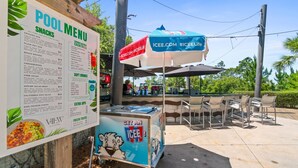 A poolside food cart with a menu listing snacks, soft drinks, and extra sips. - Beach House - Redfish Cove by PHG (Port St. Joe)
