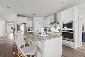 A modern kitchen with white cabinetry, a granite countertop, stainless steel appliances, and a central island with seating. - Beach House - Redfish Cove by PHG (Port St. Joe)