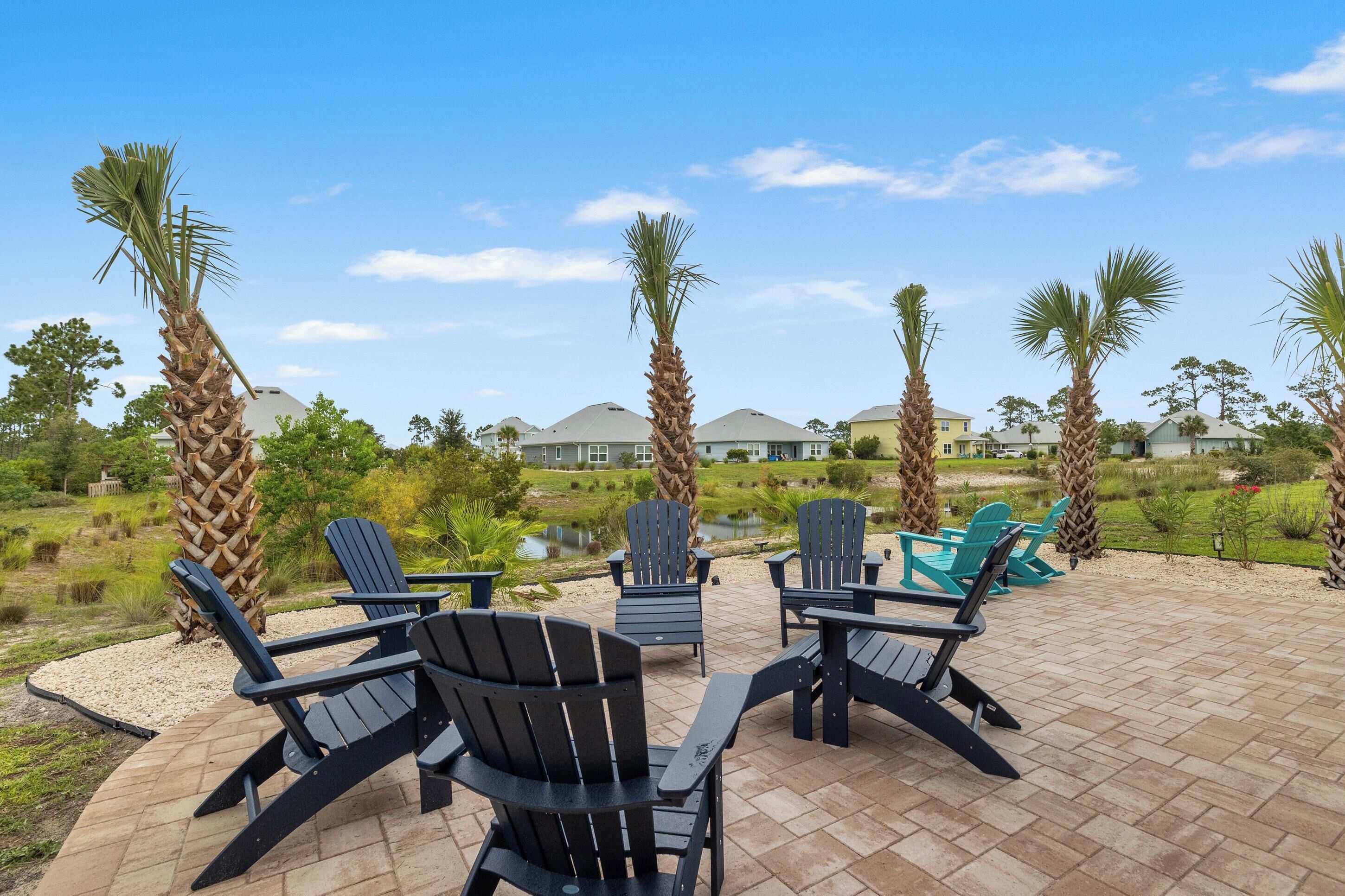 Un patio al aire libre con sillas Adirondack, un pequeño estanque y vistas de casas al fondo.