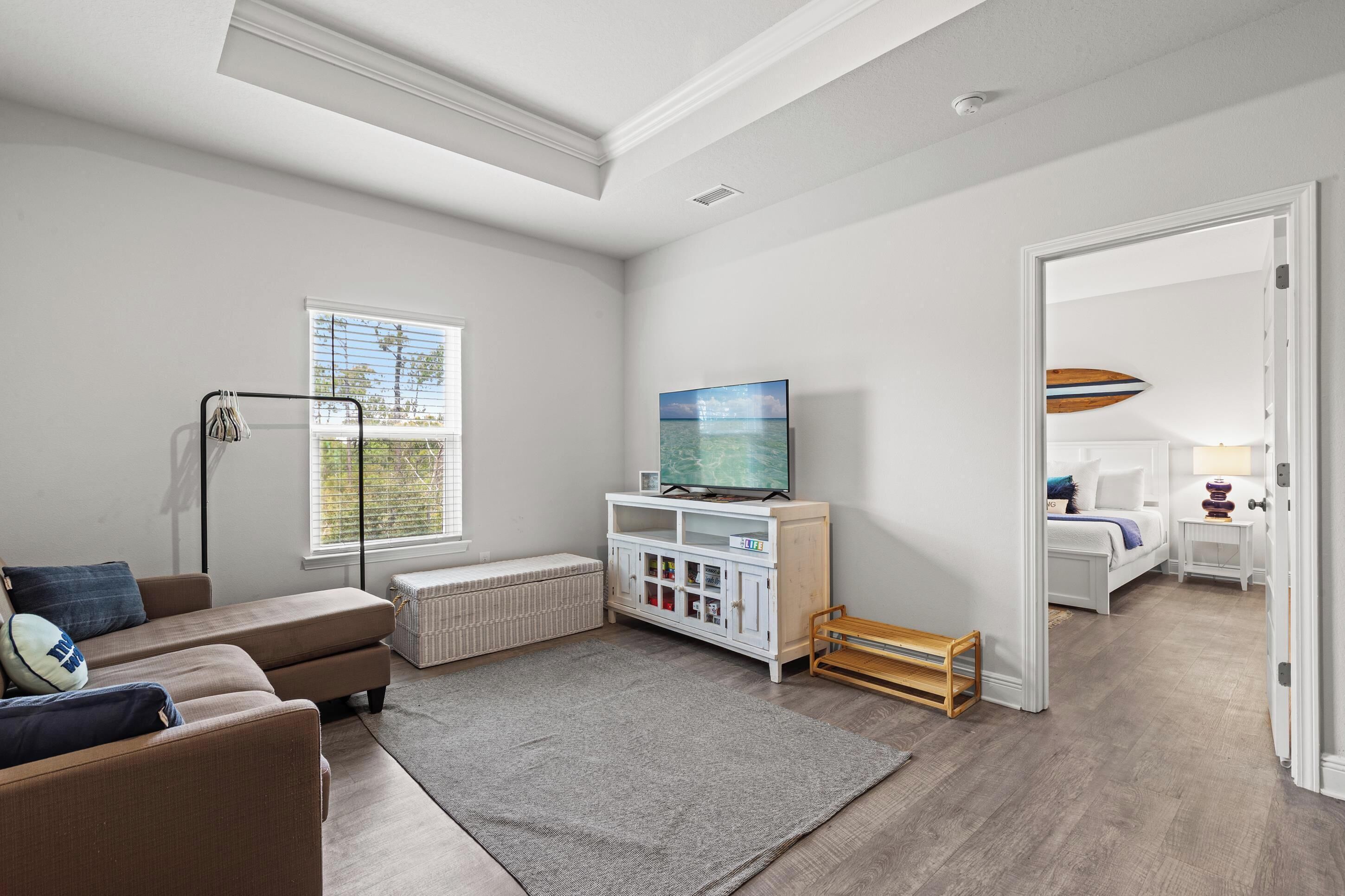 Una sala de estar moderna con un sofá, un televisor, un mueble blanco y una ventana con persianas.