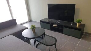 A modern living room with a large flat-screen TV, a sofa, a small round table, and a potted plant.