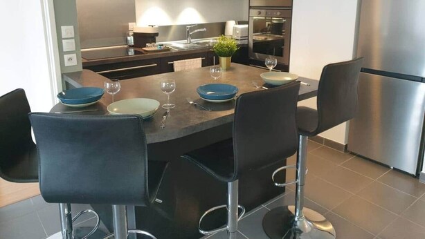A modern kitchen with a central island, stainless steel appliances, and black chairs.