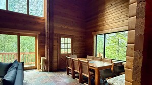 L’intérieur d’un chalet en bois comprend un coin repas, de grandes fenêtres et offre une vue sur la verdure.