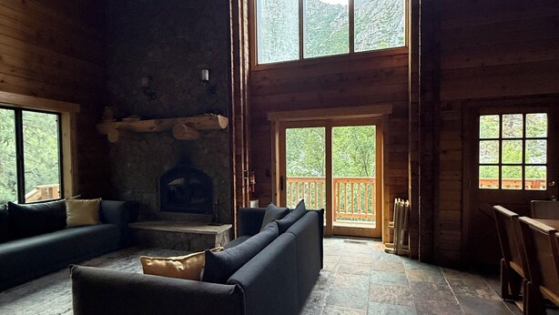 L’intérieur d’une cabane en rondins, avec une cheminée en pierre, un grand canapé et un coin repas.