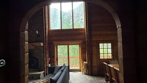 Un intérieur chaleureux de chalet en bois avec une cheminée en pierre, un canapé et un coin repas.