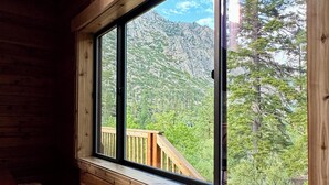 Une cabane dotée d’une grande fenêtre donnant sur un paysage de montagne et de forêt.